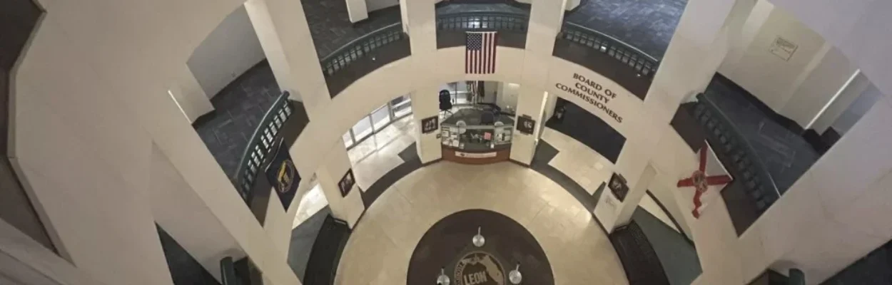 A view looking down through the open rotunda of the Leon County Courthouse in Tallahassee. On the ground floor, the county seal is embedded in the tile floor beneath an American flag hanging from the second level.