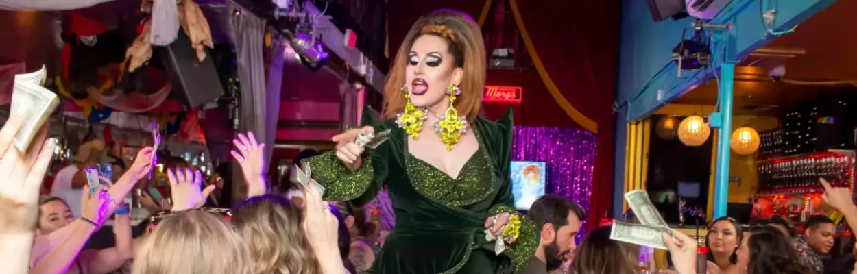 A drag performer accepts tips from audience members during a crowded show.