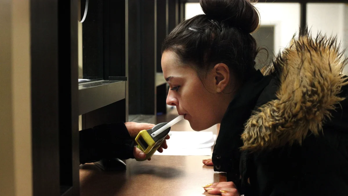 A woman in a jail blows into a Breathalyzer machine.