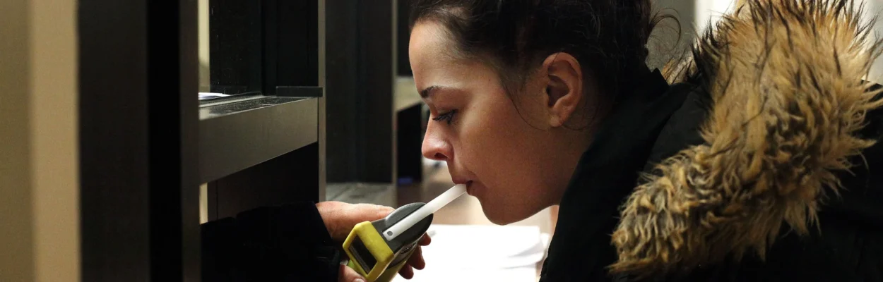 A woman in a jail blows into a Breathalyzer machine.