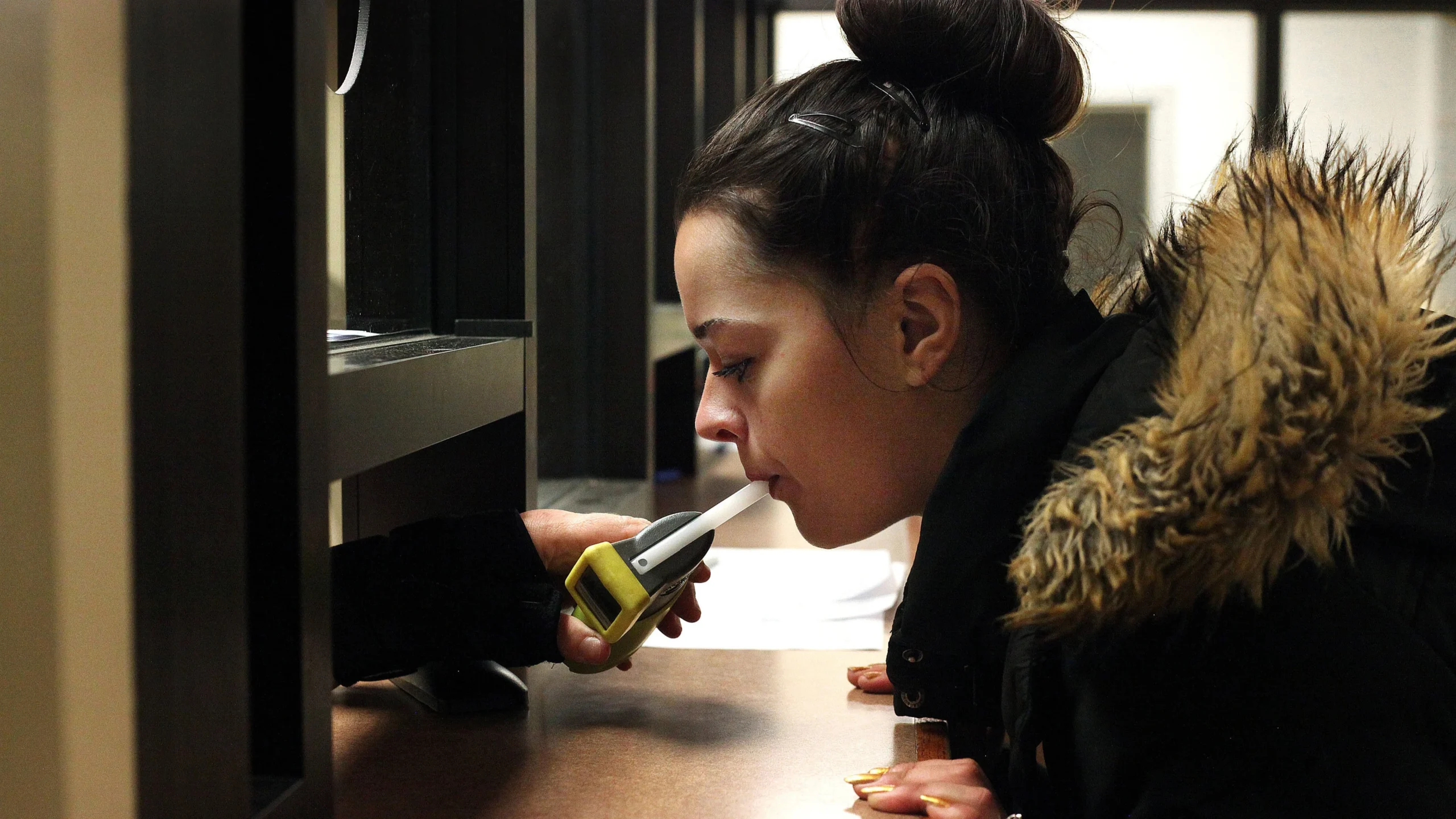 A woman in a jail blows into a Breathalyzer machine.
