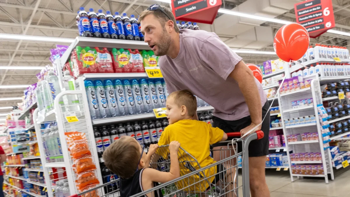Jaguars punter Logan Cooke bends over a shopping cart holding two children during a hunger event.