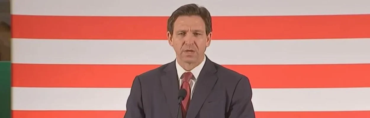 Gov. Ron DeSantis stands at a lectern with a sign that reads "Biden's Border Crisis." He approved funding for Flock cameras used in immigration enforcement.