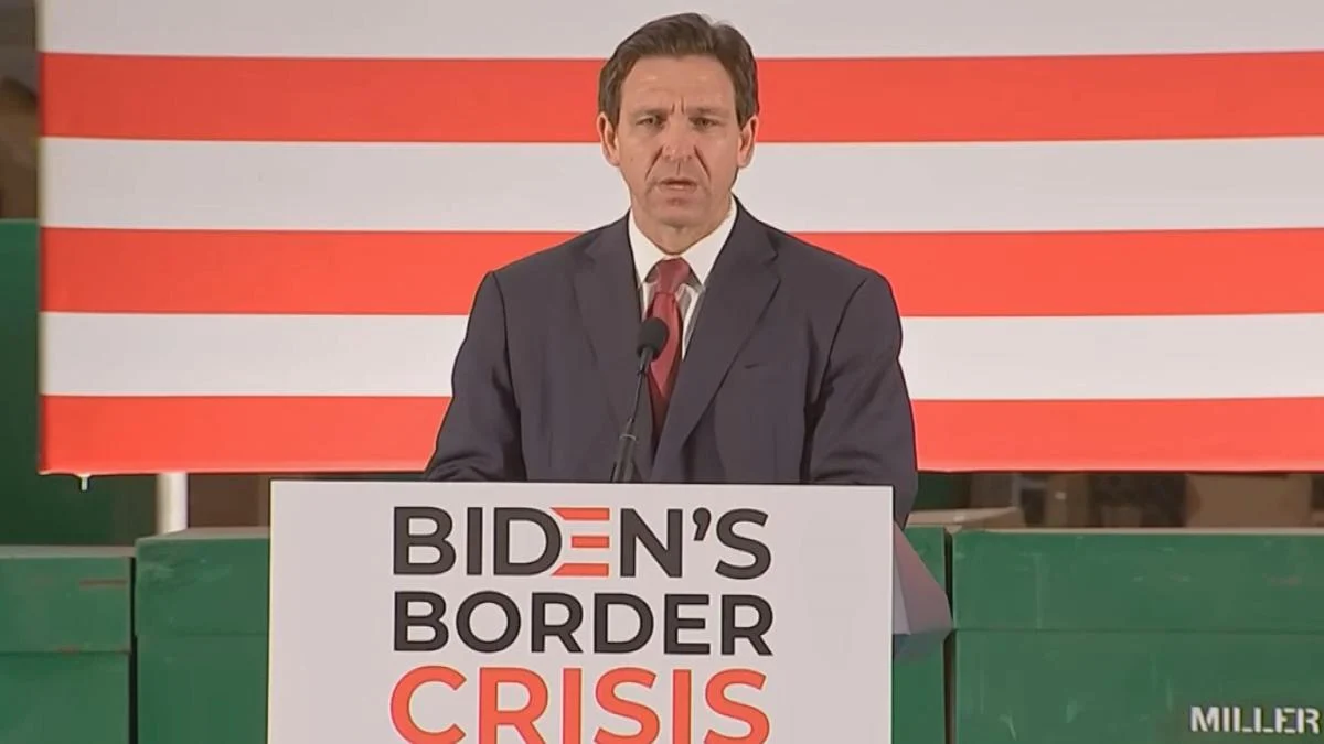 Gov. Ron DeSantis stands at a lectern with a sign that reads "Biden's Border Crisis." He approved funding for Flock cameras used in immigration enforcement.