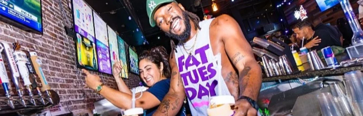 A smiling bartender hold two drinks at Fat Tuesday Social Lounge.