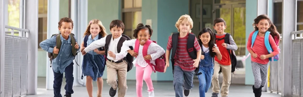 Smiling children run out of a school building.