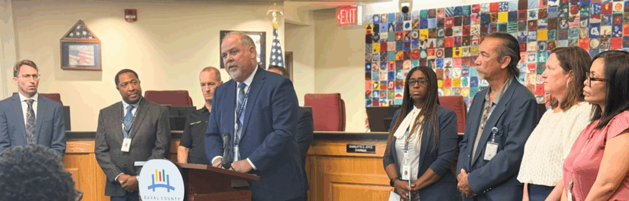 District staff stands around Superintendent Christopher Bernier, at a lectern during a press conference.