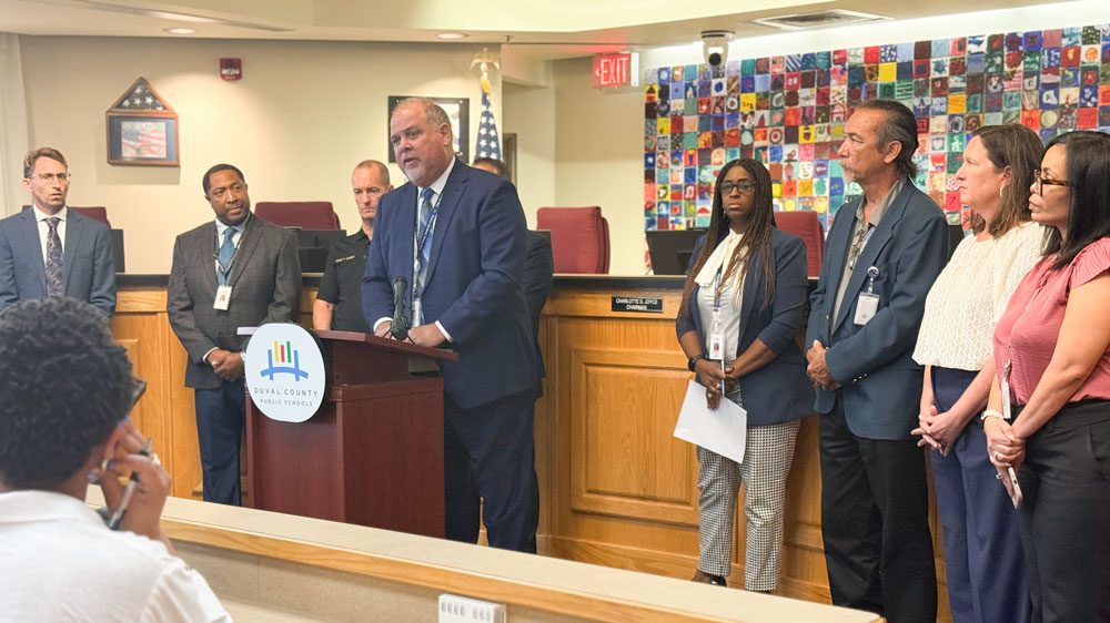 District staff stands around Superintendent Christopher Bernier, at a lectern during a press conference.