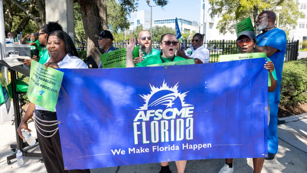 AFSCME Local 1328 and Local 1781 members hold a blue sign during a demonstration outside UF Health Jacksonville's campus in Brentwood