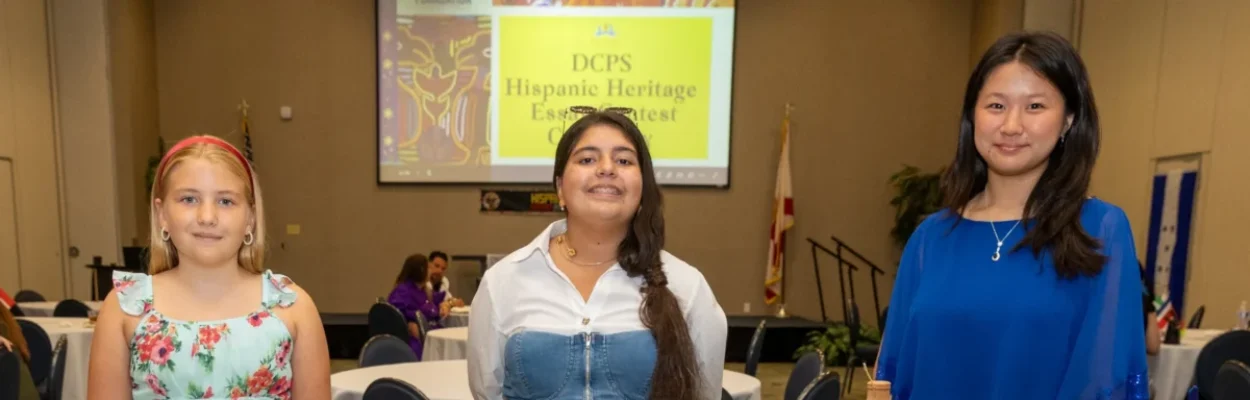 Three students stand with displays noting their winning essays in a Hispanic Heritage Month contest.