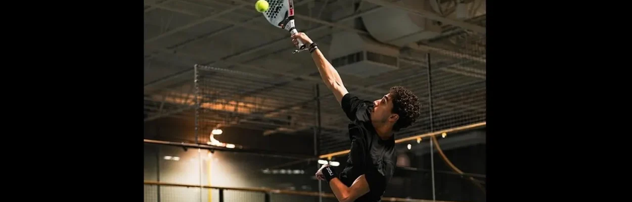 A padel player reaches over his head to hit a shot.